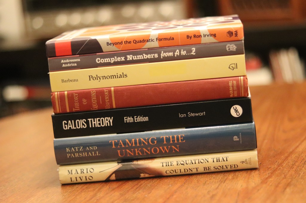 A photograph of a stack of seven small math books on a wooden table (authors and titles in post).